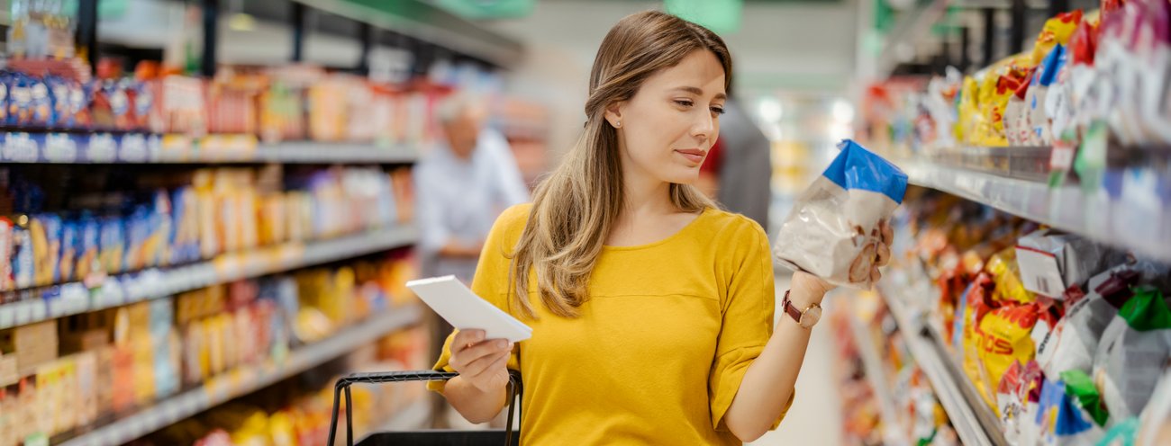 Frau in gelbem Pullover wählt Produkt im Supermarkt aus. Die Verbraucher-Plattform des Markenverbandes