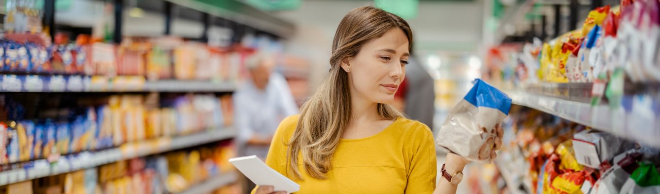 Frau in gelbem Pullover wählt Produkt im Supermarkt aus. Die Verbraucher-Plattform des Markenverbandes